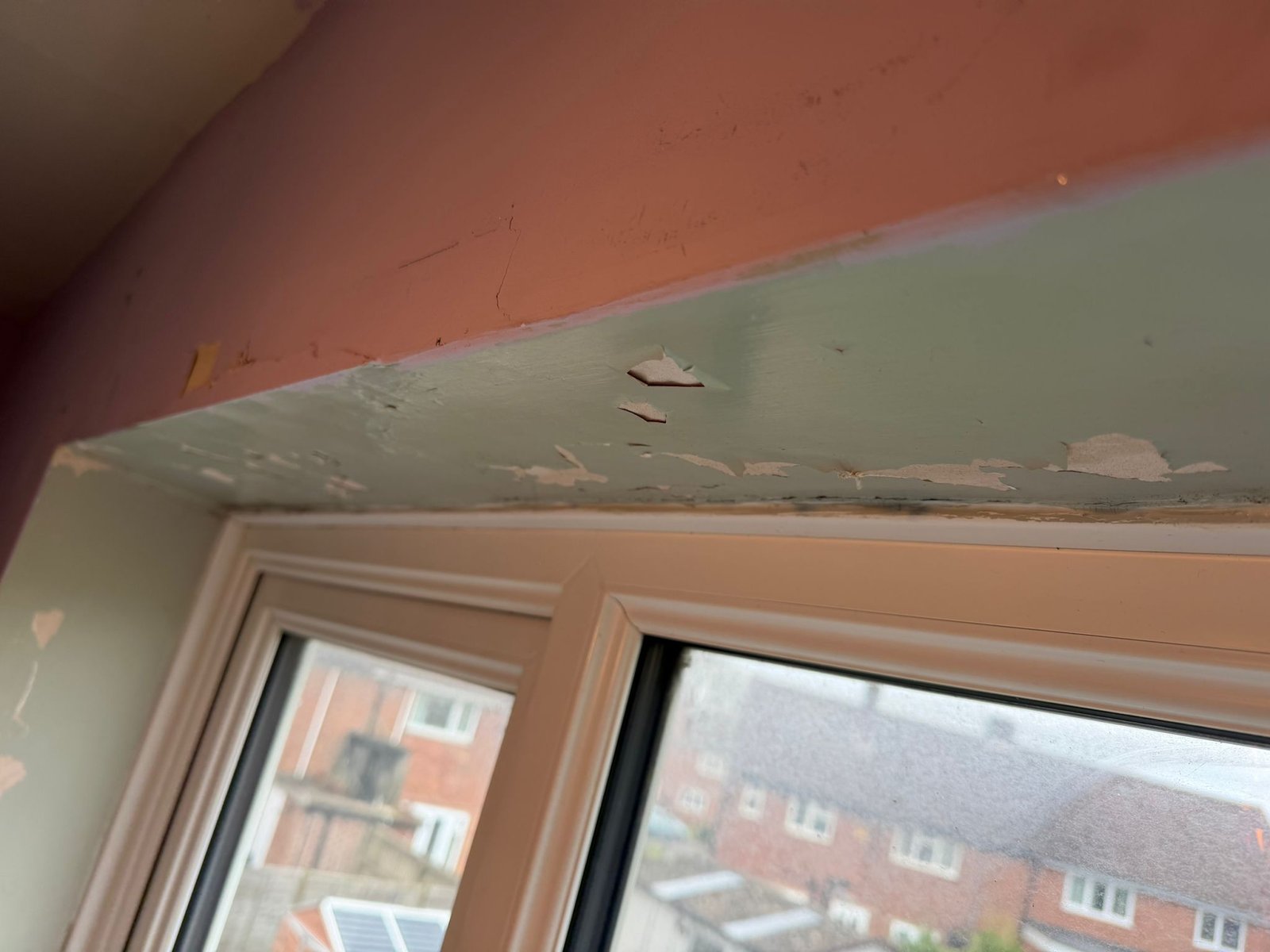 A wall above a window cracked and peeling paint